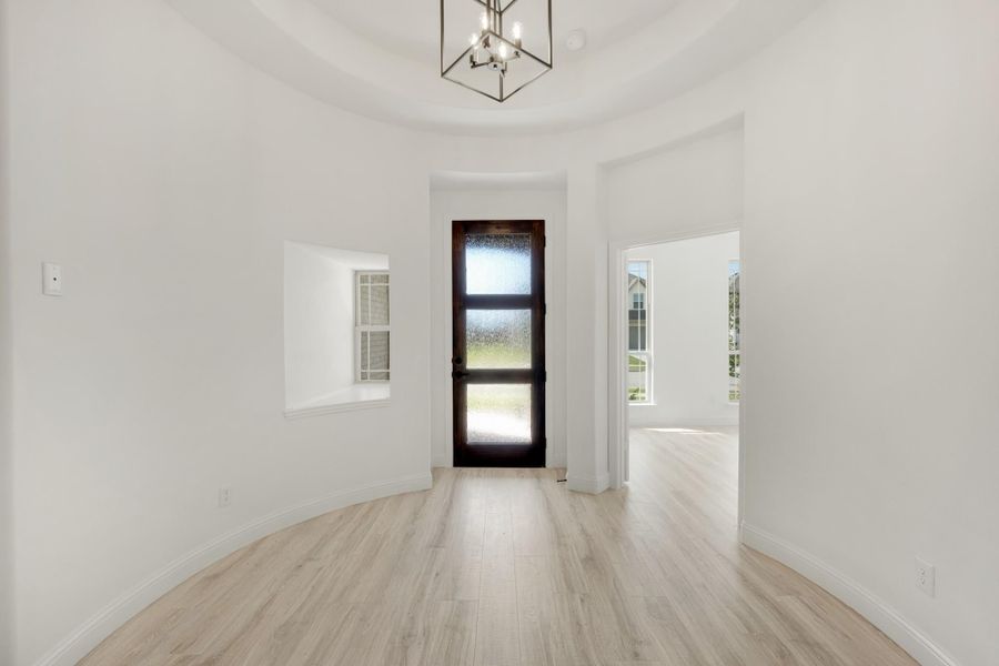 Round foyer with tray ceiling, chandelier, dark wood front door, and light hardwood floors