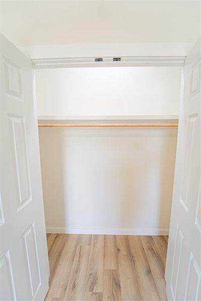 Wardrobe closet featuring a light wood-finish flooring, white baseboards, and a single wooden clothing rod