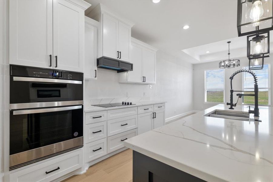 Kitchen featuring double oven, white cabinetry, a sink, and premium range hood