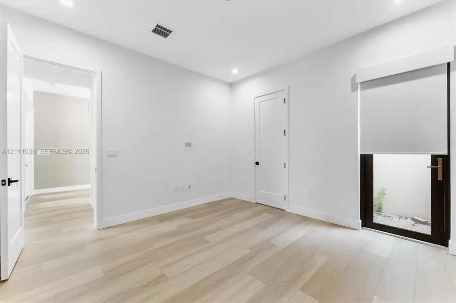 Neutral-toned interior featuring wood-finish flooring, recessed lighting, shaker-style doors with matte black hardware, and an exterior door with integrated window and blind