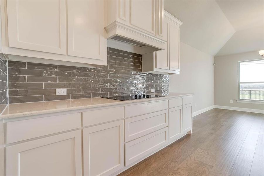 Kitchen with light hardwood / wood-style flooring, backsplash, white cabinetry, custom range hood, and black electric stovetop