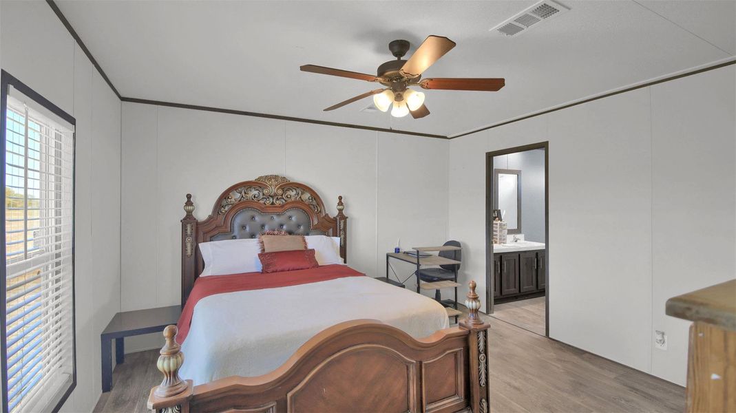 Bedroom with wood finished floors, a ceiling fan, ensuite bathroom, and ornamental molding