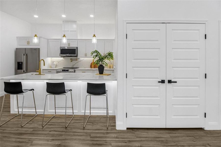 Kitchen featuring white cabinetry, a kitchen breakfast bar, appliances with stainless steel finishes, dark wood-style flooring, and hanging light fixtures Kitchen featuring white cabinetry, a kitchen breakfast bar, appliances with stainless steel finishes, dark wood-style flooring, and hanging light fixtures
