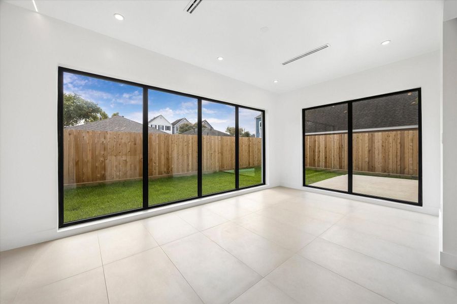 Bright and airy family room with expansive floor-to-ceiling windows offering views of a lush, fenced backyard. Bright and airy family room with expansive floor-to-ceiling windows offering views of a lush, fenced backyard.