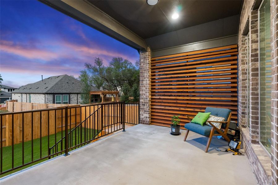 Covered patio with concrete flooring, brick columns, and a slatted wood-panel accent wall