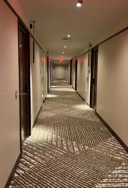 Hallway featuring geometric patterned carpeting, recessed ceiling lighting, wall-mounted sconces, and wooden door frames