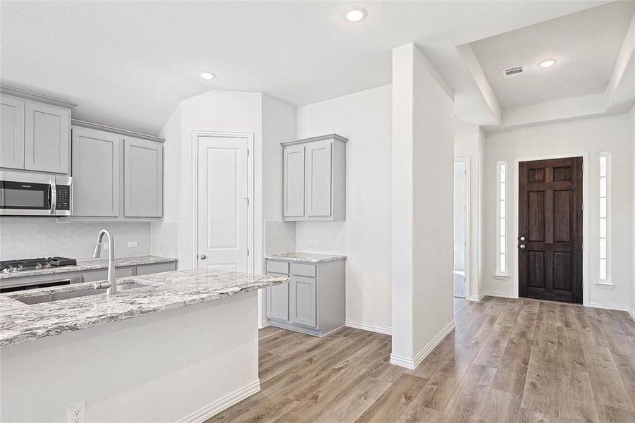 Kitchen featuring light wood-type flooring, light stone counters, sink, gray cabinetry, and stainless steel appliances