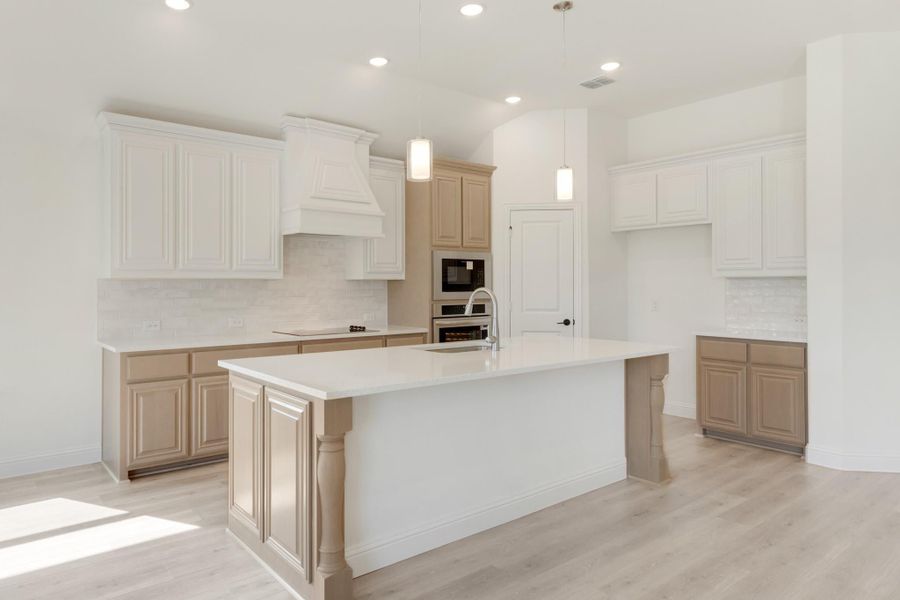 Kitchen with large center island, white upper cabinets, tan lower cabinets, and stainless steel appliances on light hardwood floors