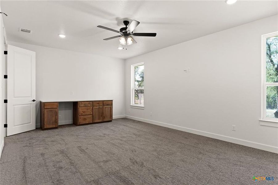 Empty room with light colored carpet, recessed lighting, ceiling fan, and built in desk