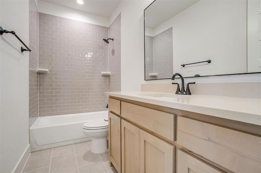 Full bathroom featuring vanity, tiled shower / bath combo, toilet, and tile patterned floors