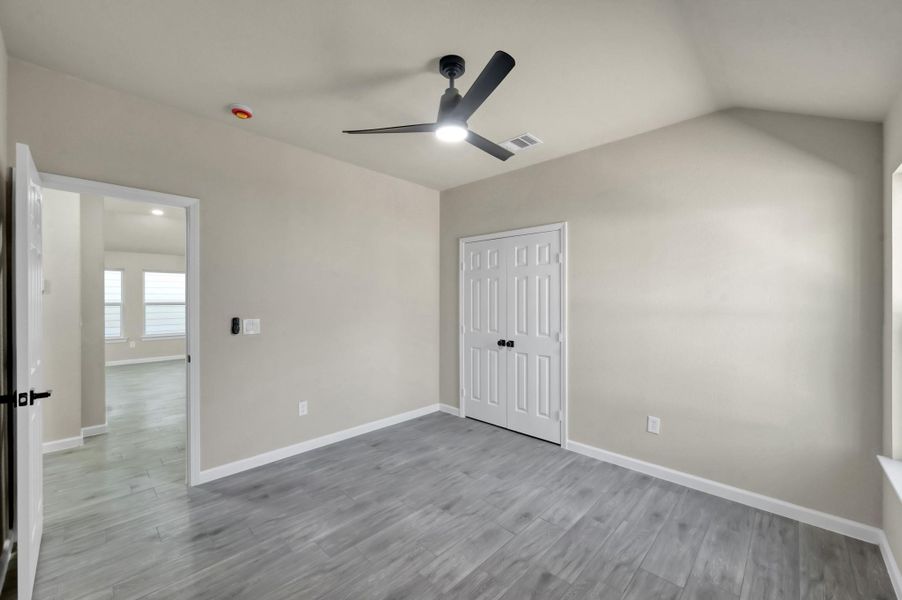 Consistency meets style in this second bedroom, featuring a large double-door closet, vaulted ceilings, and premium wood-look laminate flooring that flows seamlessly throughout the home.