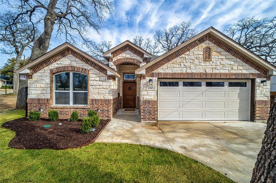 View of front of house featuring brick siding, a front yard, a garage, stone siding, and driveway