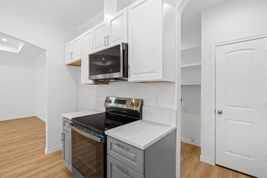 Kitchen featuring appliances with stainless steel finishes, ornamental molding, light wood-style floors, gray cabinets, and white cabinets Kitchen featuring appliances with stainless steel finishes, ornamental molding, light wood-style floors, gray cabinets, and white cabinets