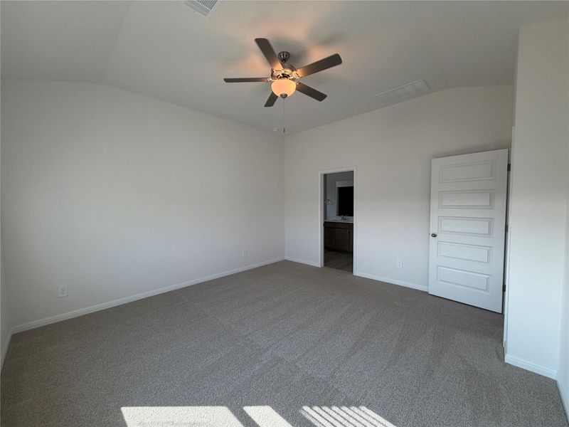 Unfurnished bedroom with vaulted ceiling, ensuite bathroom, carpet, and ceiling fan