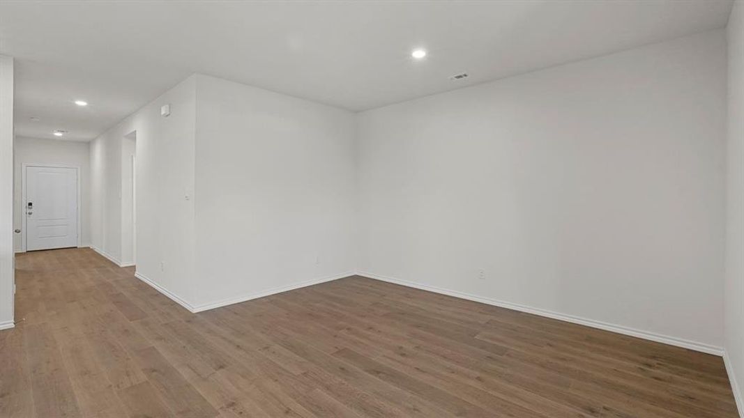 Spacious room featuring wood-finish flooring, recessed lighting, white baseboards, and a white paneled door