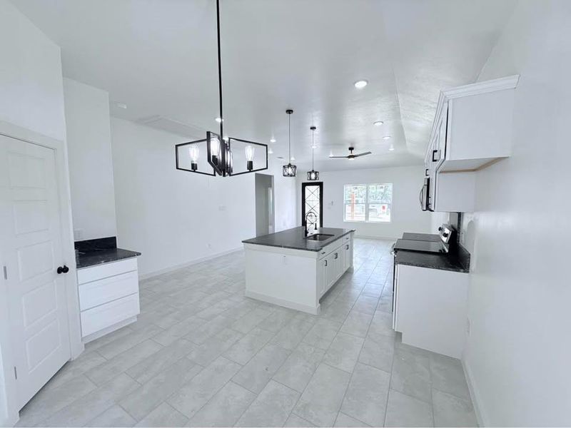 Kitchen with an island with sink, white cabinetry, hanging light fixtures, a chandelier, and recessed lighting Kitchen with an island with sink, white cabinetry, hanging light fixtures, a chandelier, and recessed lighting