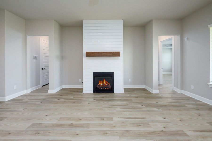 Step into the heart of the home—this inviting living room features a cozy fireplace with shiplap surround and rustic wood mantle, perfectly framed by neutral tones and wide-plank luxury vinyl flooring. Open to the kitchen, it's an ideal space for entertaining or relaxing, with seamless flow and natural light.