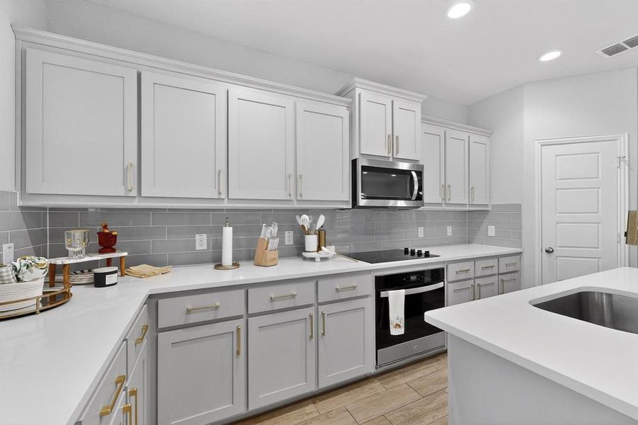 The kitchen features light grey cabinetry with gold-toned hardware, white countertops, and a grey subway tile backsplash