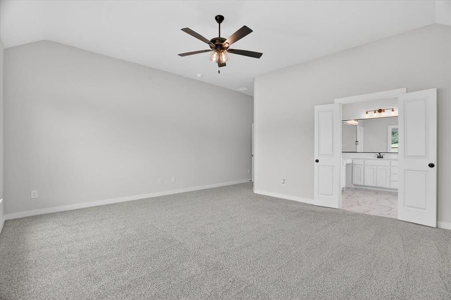 Spacious carpeted room featuring vaulted ceilings and a ceiling fan with light fixture