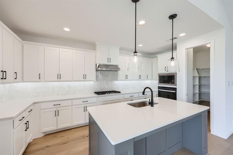 Kitchen with white cabinetry, stainless steel appliances, hanging light fixtures, and sink