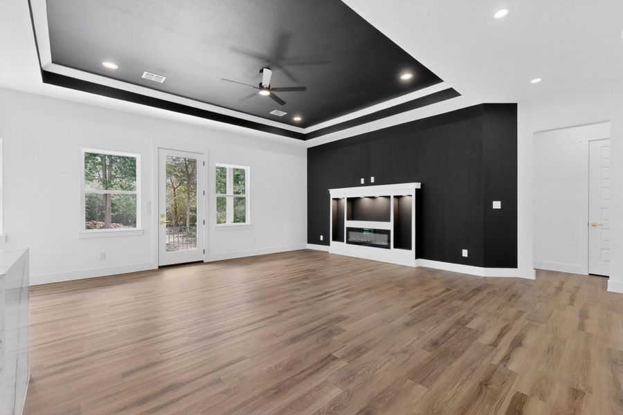 A spacious, naturally illuminated room boasts hardwood flooring and a stylish black tray ceiling with recessed lighting.