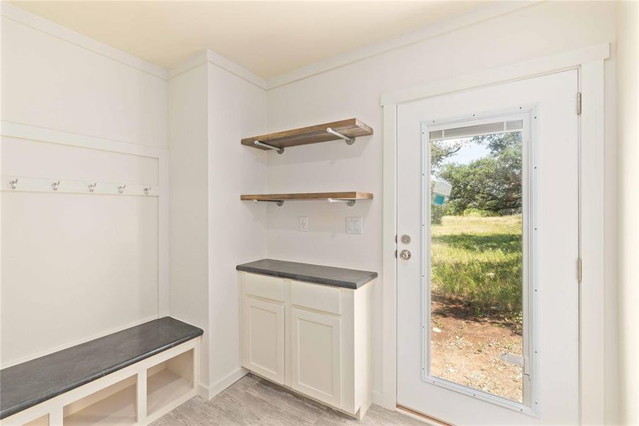 Entryway featuring a built-in bench with cubbies, wall-mounted coat hooks, and floating wood shelves