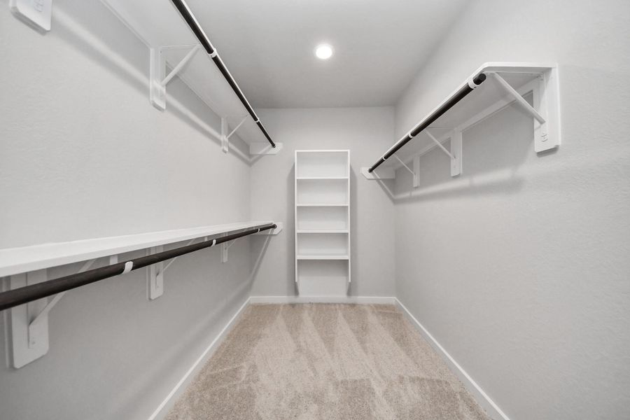 Walk-in closet that epitomizes luxury and practicality. This generously sized space features built-in shelving, offering abundant room for impeccable organization. High ceilings and recessed lighting create a bright and welcoming ambiance. Sample photo of completed home with similar floor plan. Actual colors and selections may vary.