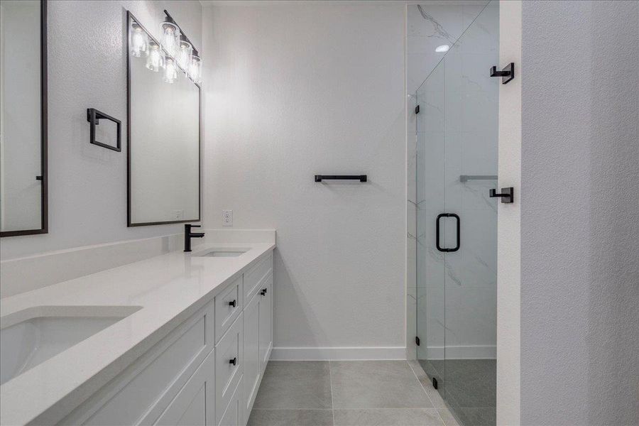 Additional view of the primary bathroom featuring a double vanity and a glass-enclosed shower for daily convenience.