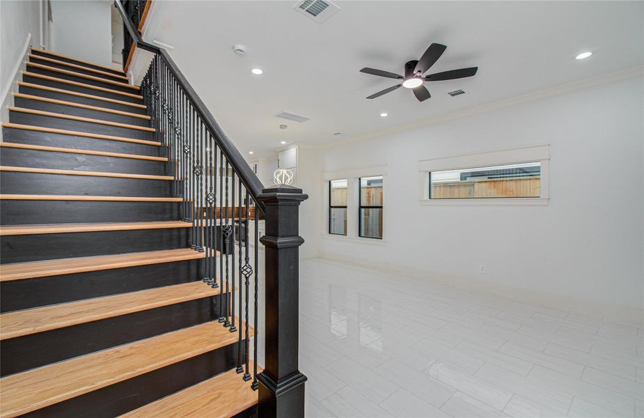 A striking staircase with dark wood steps and elegant iron railings adds character. Large windows provide natural light, enhancing the room's bright, airy feel.