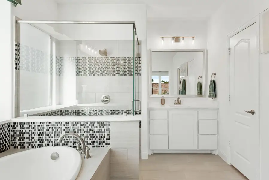 Bathroom with soaking tub, glass-enclosed shower, mosaic tile accents, and white vanity with mirror.