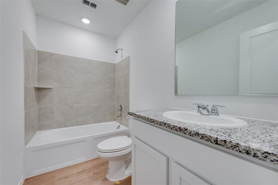 Full bathroom with vanity, hardwood / wood-style flooring, tiled shower / bath combo, and toilet