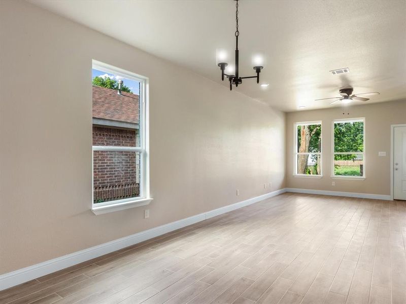 Spare room featuring healthy amount of natural light, light wood-style floors, a ceiling fan, and a chandelier Spare room featuring healthy amount of natural light, light wood-style floors, a ceiling fan, and a chandelier