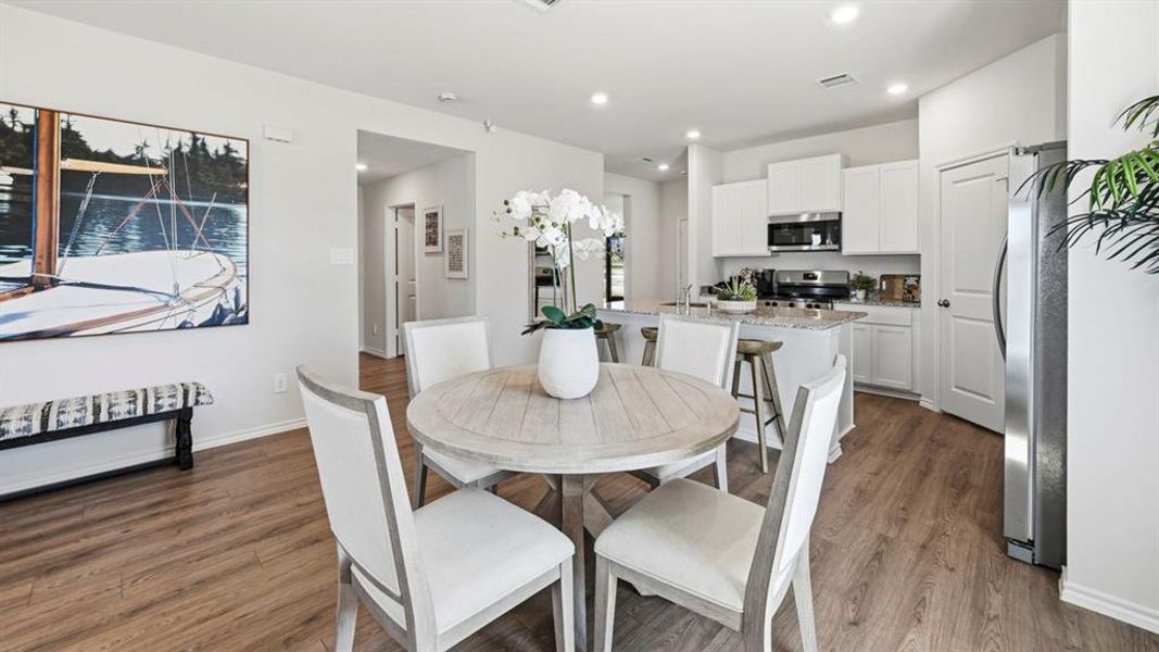 The property features a bright dining area with wood-look flooring and a round table, open to a kitchen with white cabinetry, stainless steel appliances, and a granite-topped island with seating