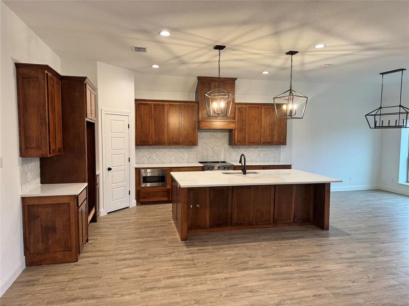 Kitchen featuring an island with sink, sink, light hardwood / wood-style floors, and decorative light fixtures
