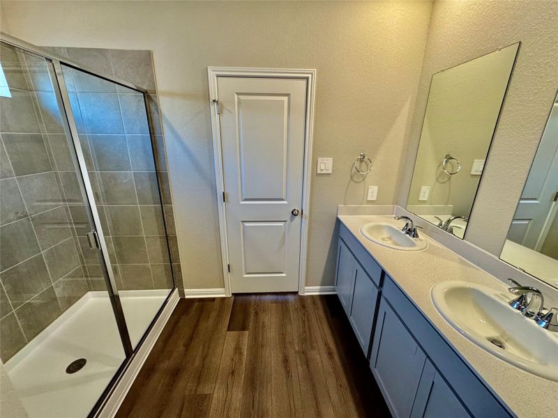 Full bath featuring double vanity, a stall shower, wood finished floors, and a textured wall Full bath featuring double vanity, a stall shower, wood finished floors, and a textured wall