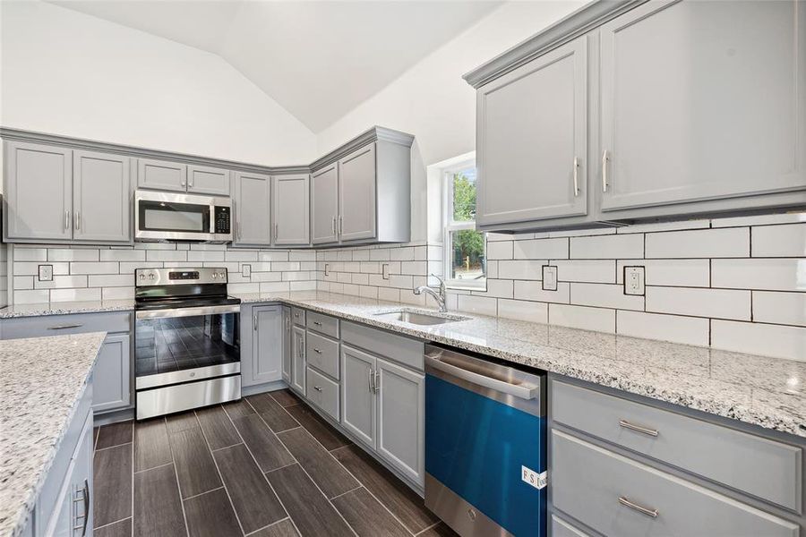 Kitchen featuring tasteful backsplash, vaulted ceiling, sink, appliances with stainless steel finishes, and gray cabinetry