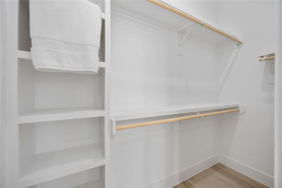 This spacious walk-in closet offers built-in shelving, double hanging rods, and bright white finishes, providing ample organized storage within a clean, functional layout. One of two walk-in closets in the primary suite.