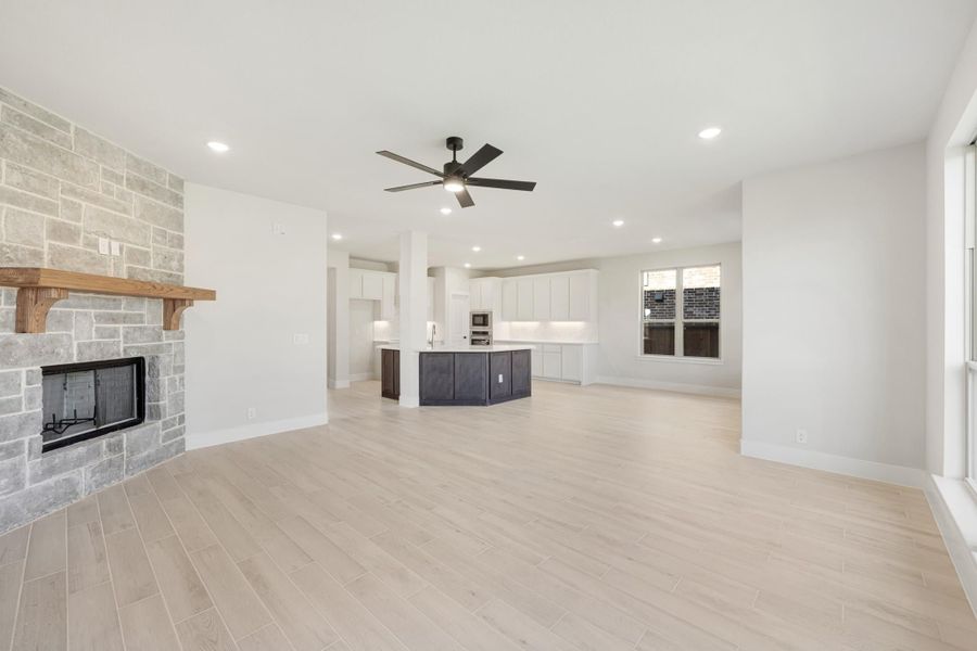 Open living area with stone fireplace, ceiling fan, and open-concept kitchen with dark island and white cabinets