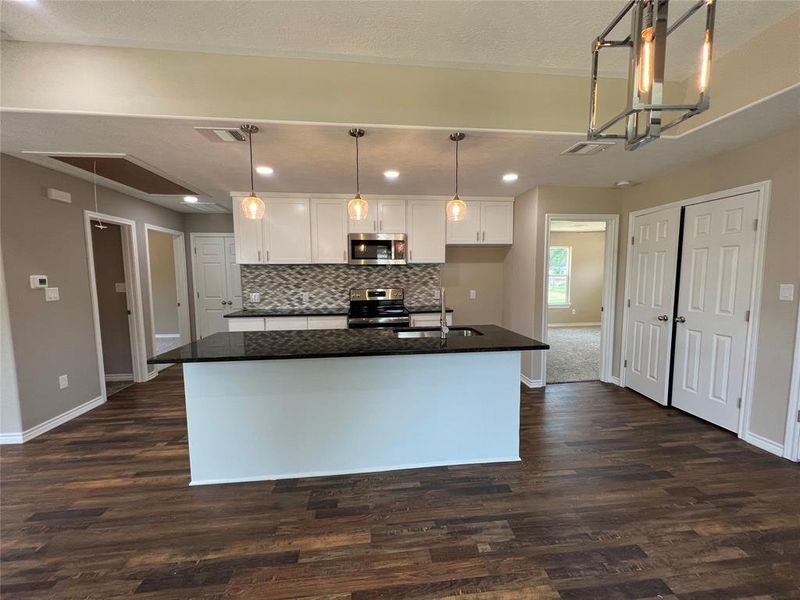 Kitchen with pendant lighting, white cabinetry, appliances with stainless steel finishes, a center island with sink, and recessed lighting