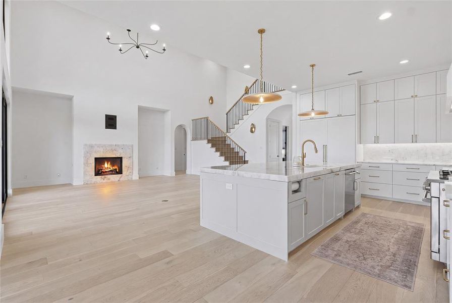 Open-concept living space featuring high ceilings, light wood-finish flooring, and a marble-surround fireplace