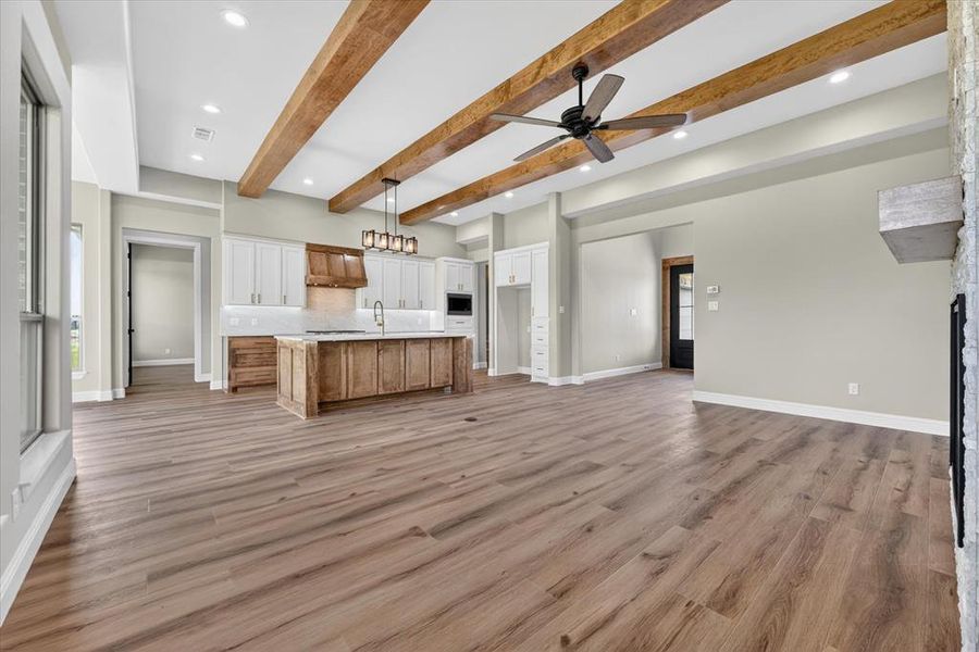 Open-concept living area featuring wood-finish flooring, exposed ceiling beams, recessed lighting, and a modern ceiling fan