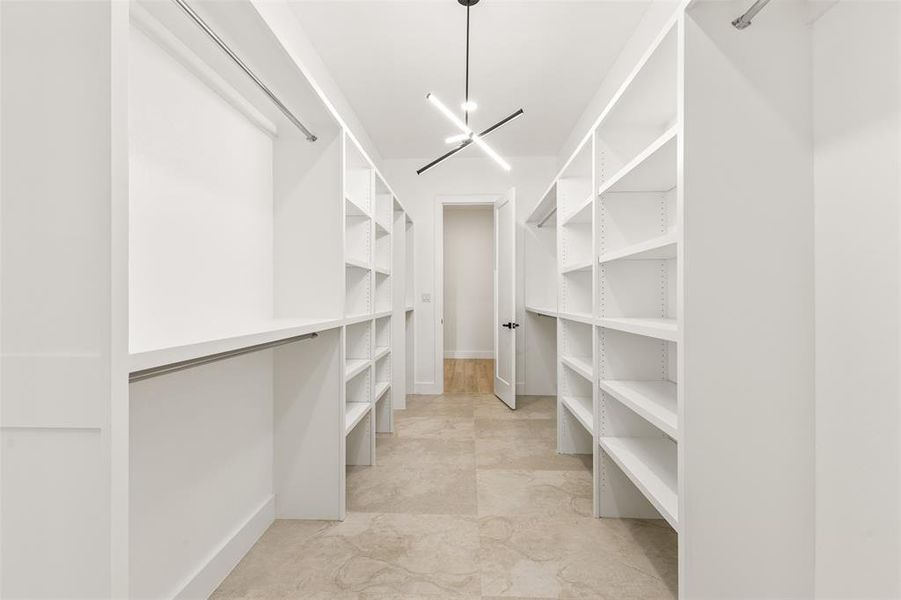 Spacious walk-in closet featuring extensive built-in shelving, hanging rods, recessed lighting, and large format tile flooring