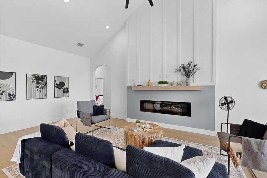 Living room featuring arched walkways, wood finished floors, high vaulted ceiling, a fireplace, and a ceiling fan