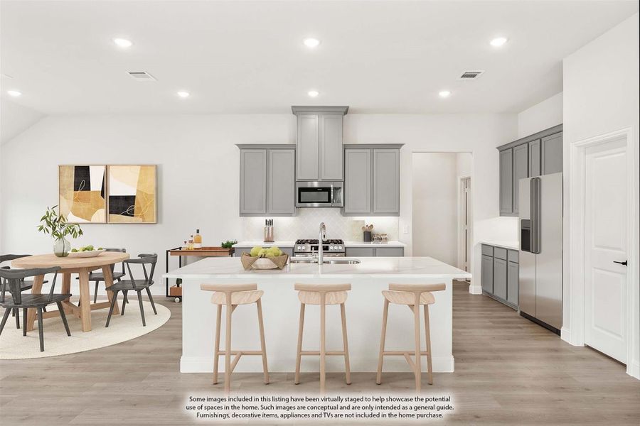 Open kitchen with gray cabinets, large center island with three bar stools, and adjacent dining area with round table. Open kitchen with gray cabinets, large center island with three bar stools, and adjacent dining area with round table.