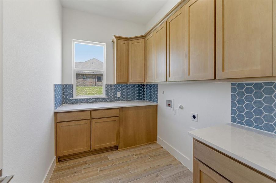 Utility room featuring light wood-finish cabinetry, white countertops, and a blue hexagonal tile backsplash