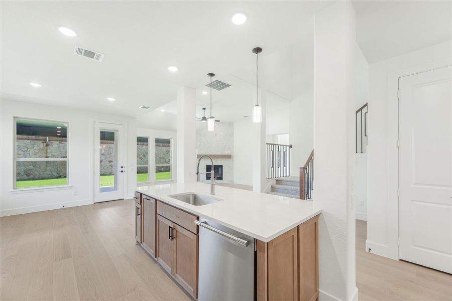 Kitchen island with sink, wood cabinets, and white countertop, open to living area with fireplace and hardwood floors Kitchen island with sink, wood cabinets, and white countertop, open to living area with fireplace and hardwood floors