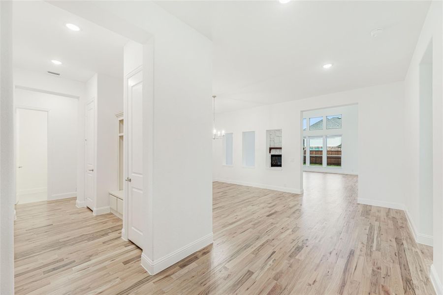 Open living area with light hardwood floors, white walls, fireplace, and chandelier in background