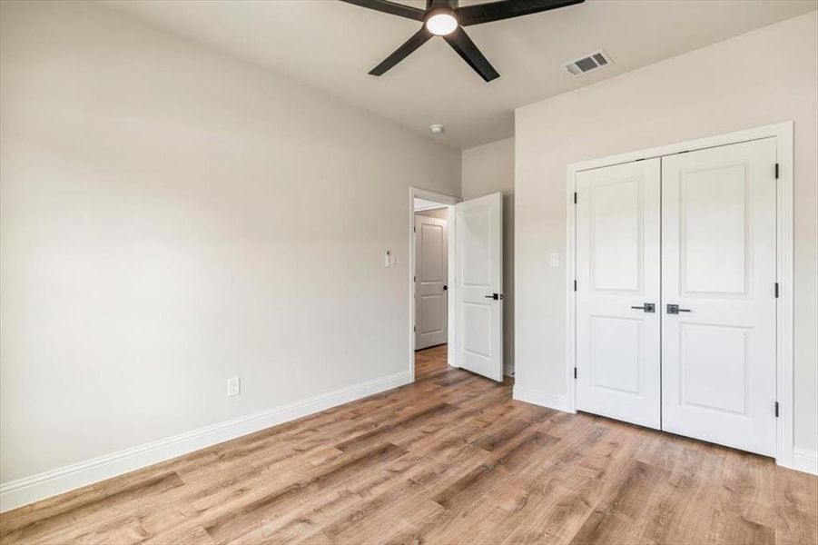 Room featuring wood-finish flooring, light-toned walls, white baseboards, and a modern black ceiling fan