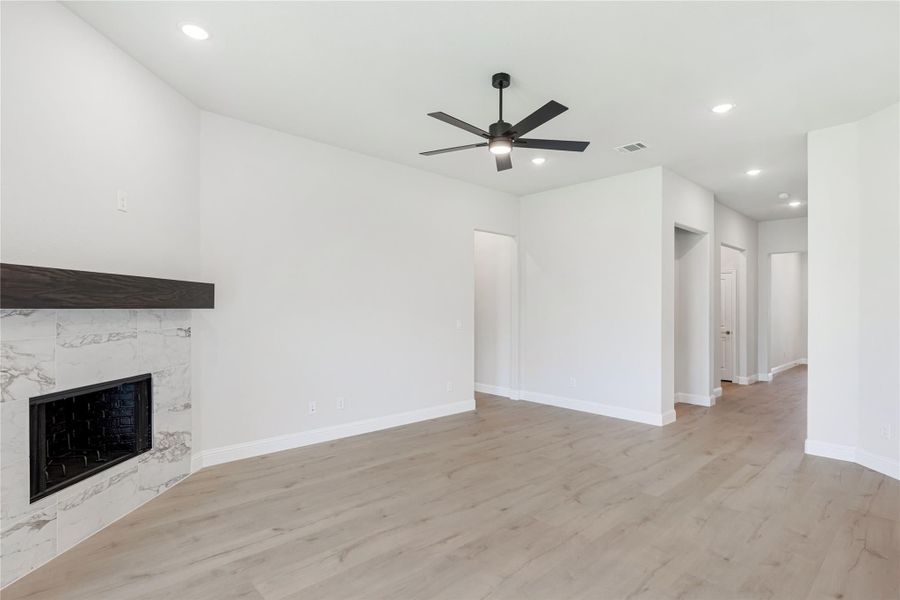 Open living room with marble tile fireplace, dark wood mantel, ceiling fan, and light hardwood floors