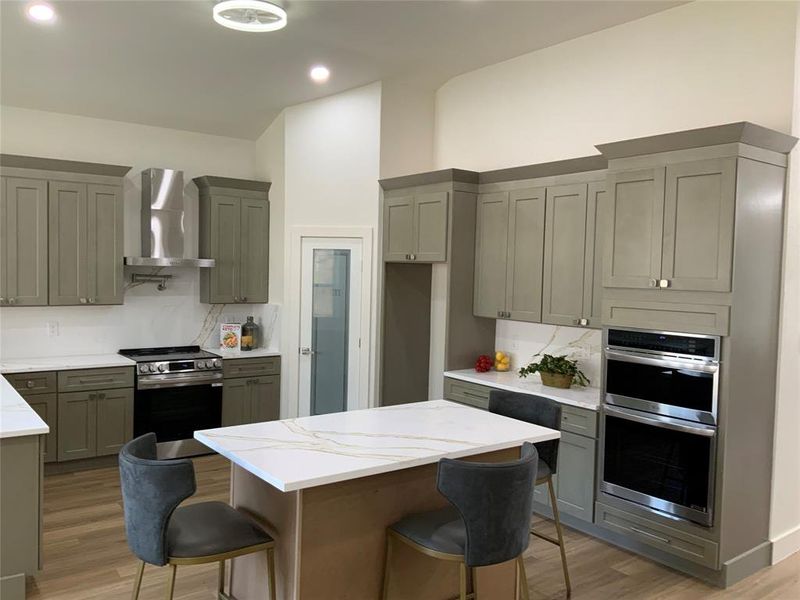 Kitchen with a breakfast bar area, light wood finished floors, decorative backsplash, stainless steel appliances, and light stone countertops Kitchen with a breakfast bar area, light wood finished floors, decorative backsplash, stainless steel appliances, and light stone countertops